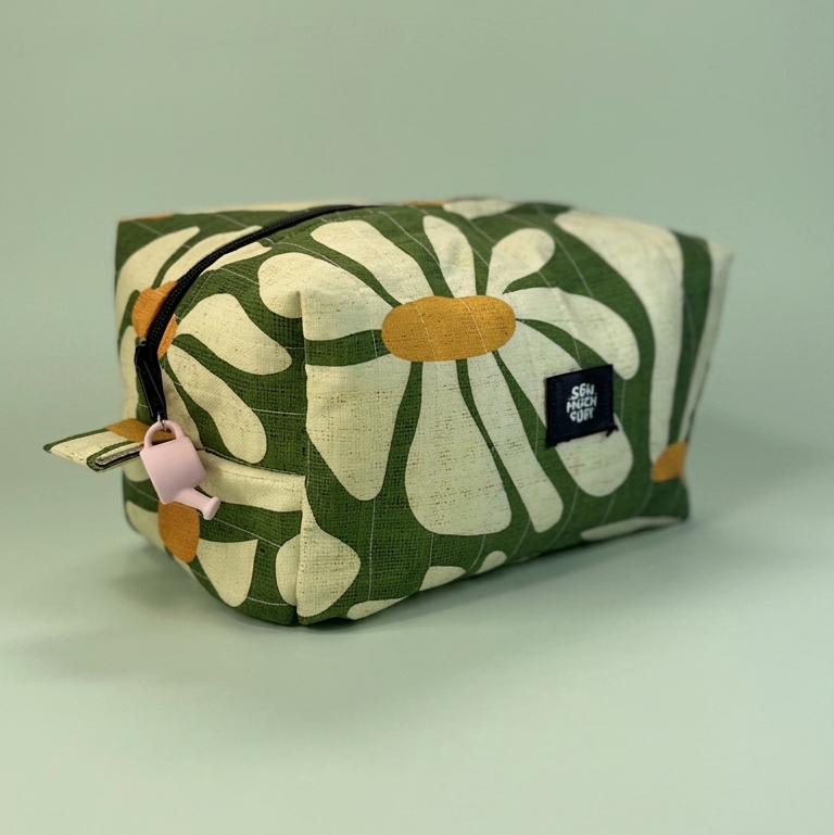 A fabric cosmetic pouch with a green and cream floral pattern, featuring a black zipper, a light pink pull tab, and a black brand label that reads 'STRAIGHT FORWARD'.