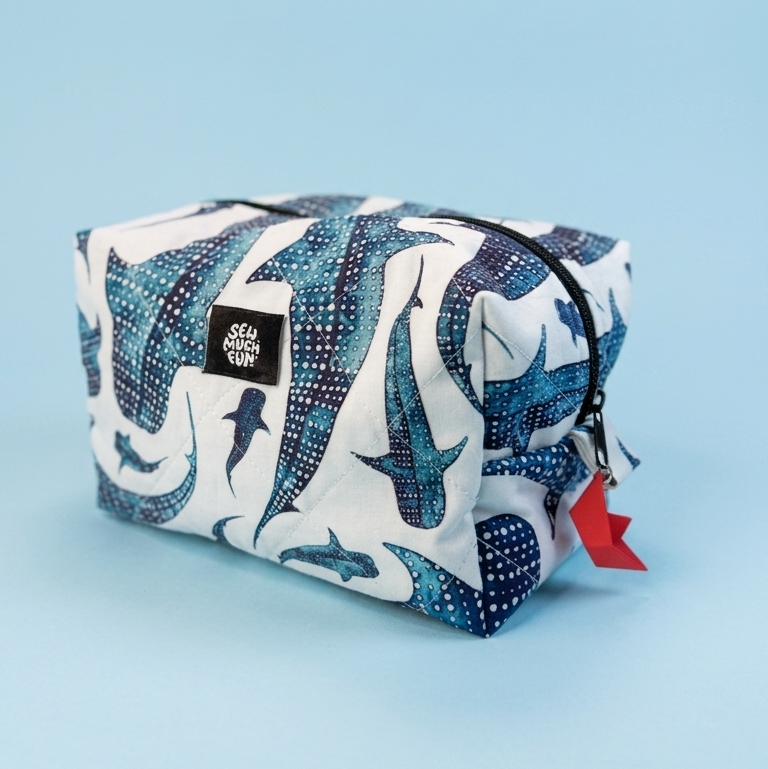 A zippered cosmetic pouch featuring a white background with a blue and navy shark pattern, shown on a solid light blue background.