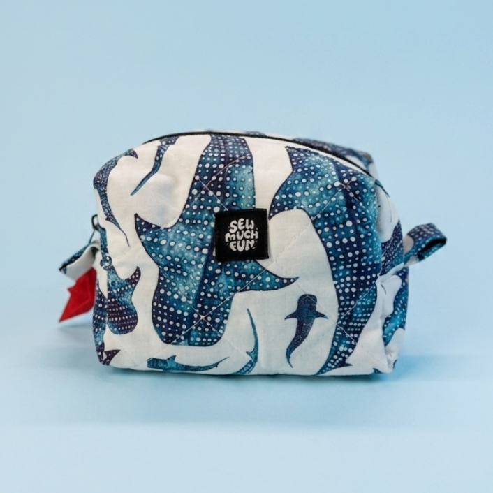 A small zippered pouch with a blue and white abstract pattern, featuring a black brand label that reads 'SELL IT OUT' and a small red zipper pull, set against a solid light blue background.