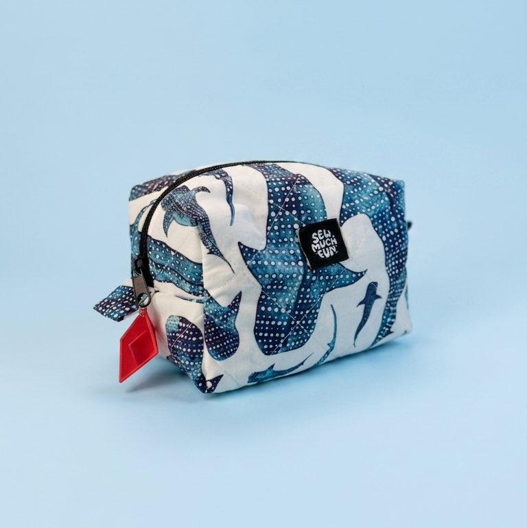 A small zippered pouch with a blue, white, and navy abstract pattern, featuring a red hangtag and a black brand label, set against a solid light blue background.